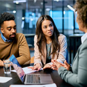 Three businesspeople talking to each other around a laptop at an office.